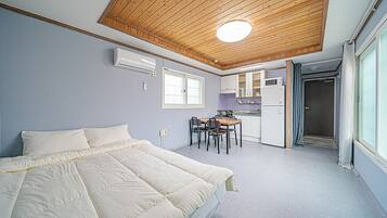 A bedroom with a large bed, a small kitchen area with a table and chairs, and a door leading to a bathroom.