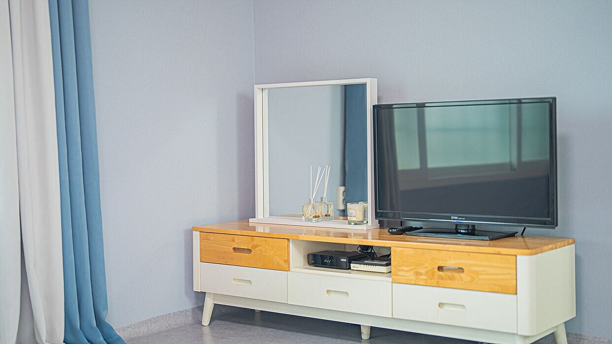 A modern bedroom with a TV, a mirror, and a wooden dresser with drawers.
