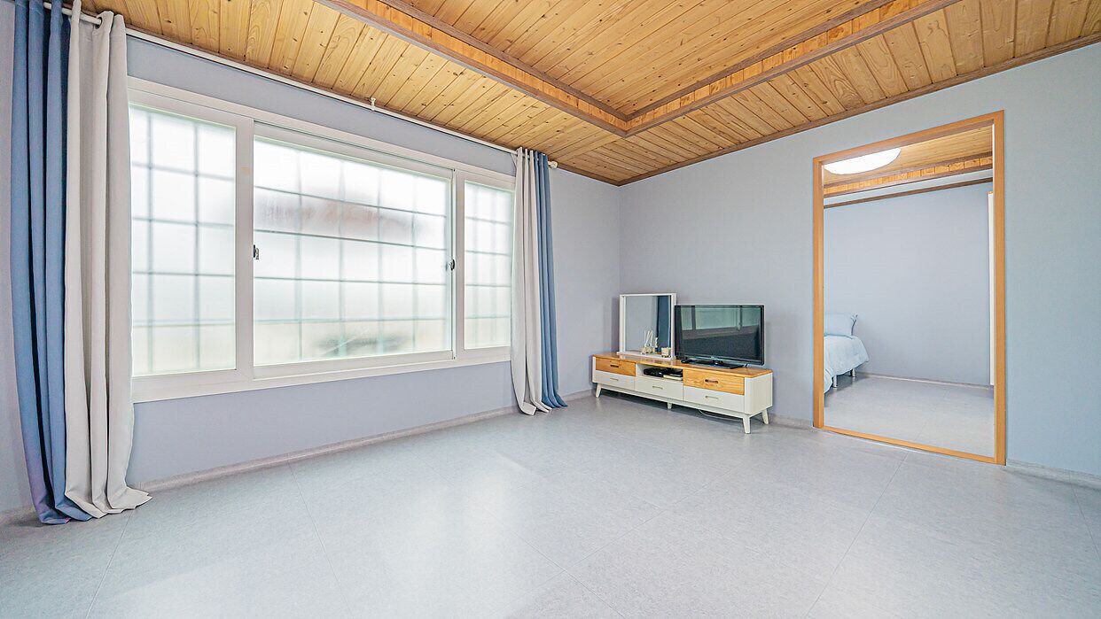 A room with a large window, a television, a mirror, and a wooden ceiling.