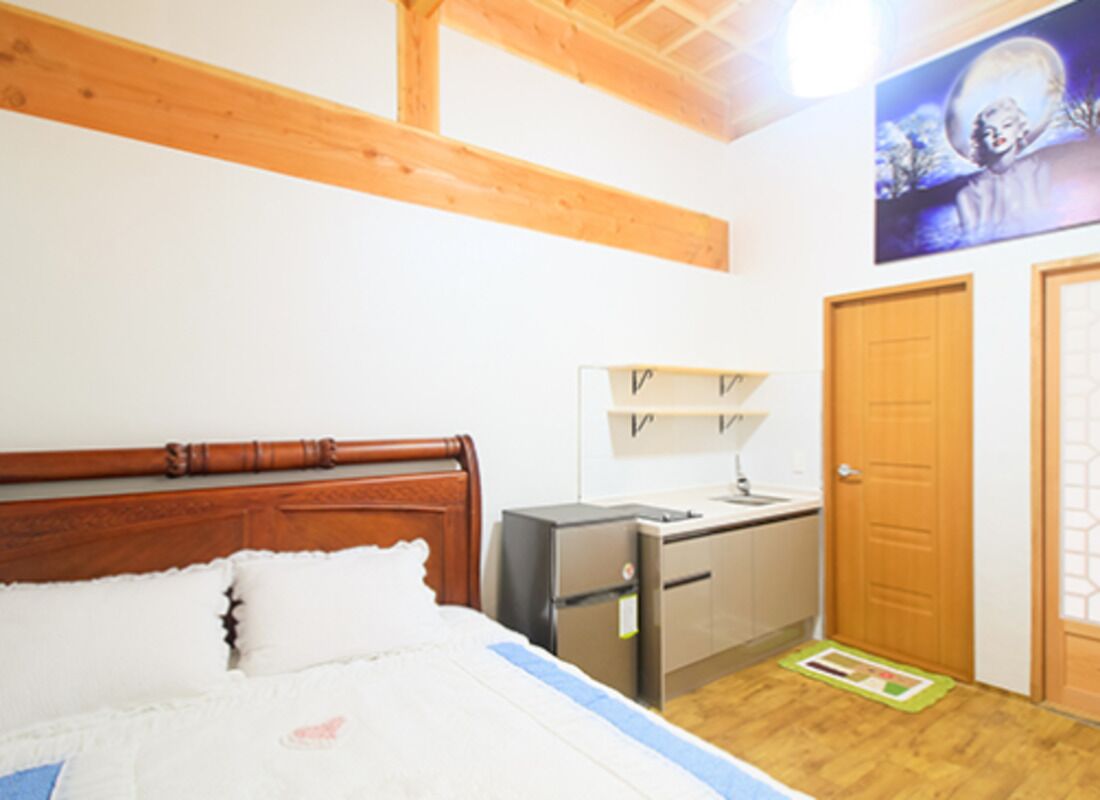 A bedroom with a wooden bed, a small kitchenette, and a door.