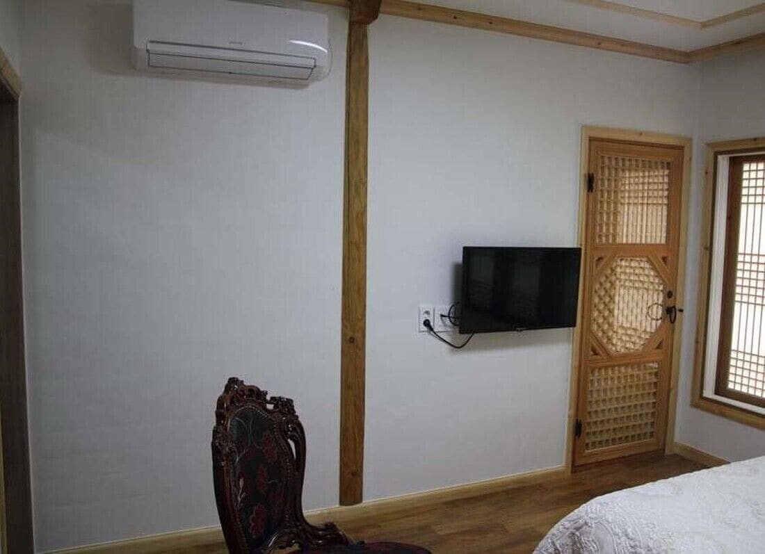 Een kamer met een bed, een aan de muur bevestigde televisie, een traditionele houten deur en een airconditioning.