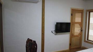 Een kamer met een bed, een aan de muur bevestigde televisie, een traditionele houten deur en een airconditioning.