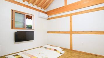 A room with wooden beams, a window, a flat-screen TV, and a quilt on the floor.