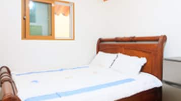 Une chambre avec un lit en bois, du linge de lit blanc, une fenêtre avec un rideau et un réfrigérateur.