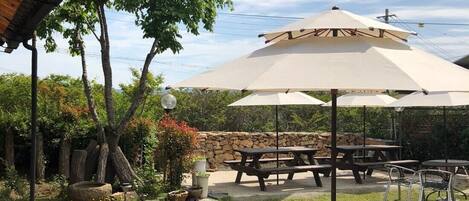 An outdoor patio area with picnic tables and umbrellas, surrounded by a stone wall and greenery.