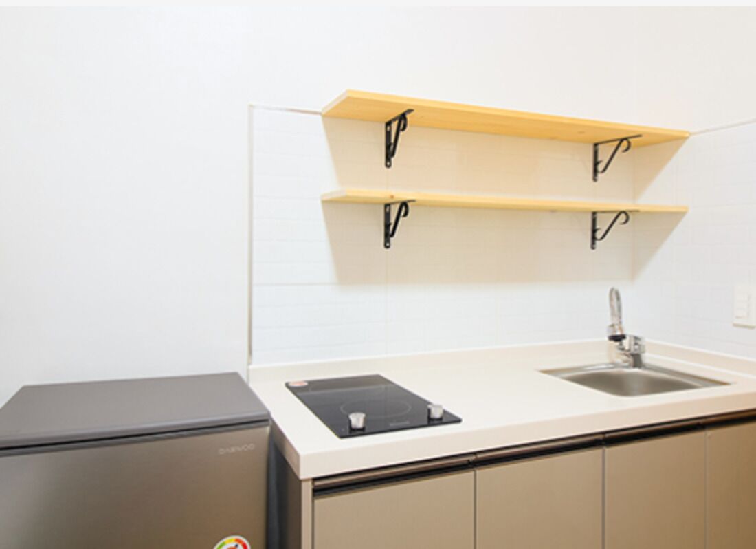 A compact kitchen with a built-in sink, a black refrigerator, and two wooden shelves above the countertop.