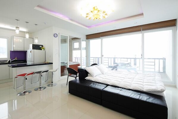 A modern bedroom with a large bed, a small kitchenette, and a balcony with a view. - Pohang Sea Shore Pension (Pohang)