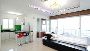 Une chambre d’hôtel moderne dotée d’une kitchenette, d’un lit et de grandes fenêtres offrant une vue dégagée.