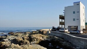 Un bâtiment moderne, de couleur blanche, doté d’un balcon, situé près d’une côte rocheuse et offrant une vue sur la mer.