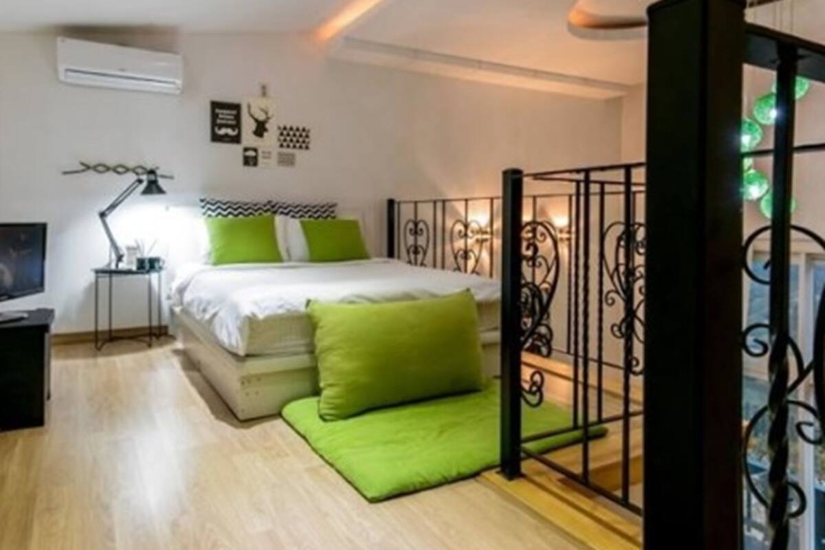 Un dormitorio con cama, mesita de noche, lámpara y ventana con detalles decorativos.