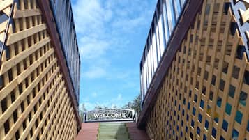 Una escalera de madera que sube hacia un edificio con un letrero que dice 'WELCOME', rodeado de paneles de celosía y ventanas de vidrio.