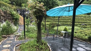 A garden pathway with stepping stones, a tree, and a table with chairs. - Emotion Pension (Hadong)
