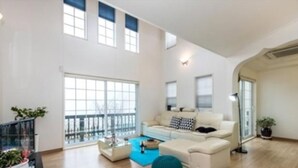 A spacious living room with a large window, a sofa, a coffee table, and a potted plant. - Emotion Pension (Hadong)