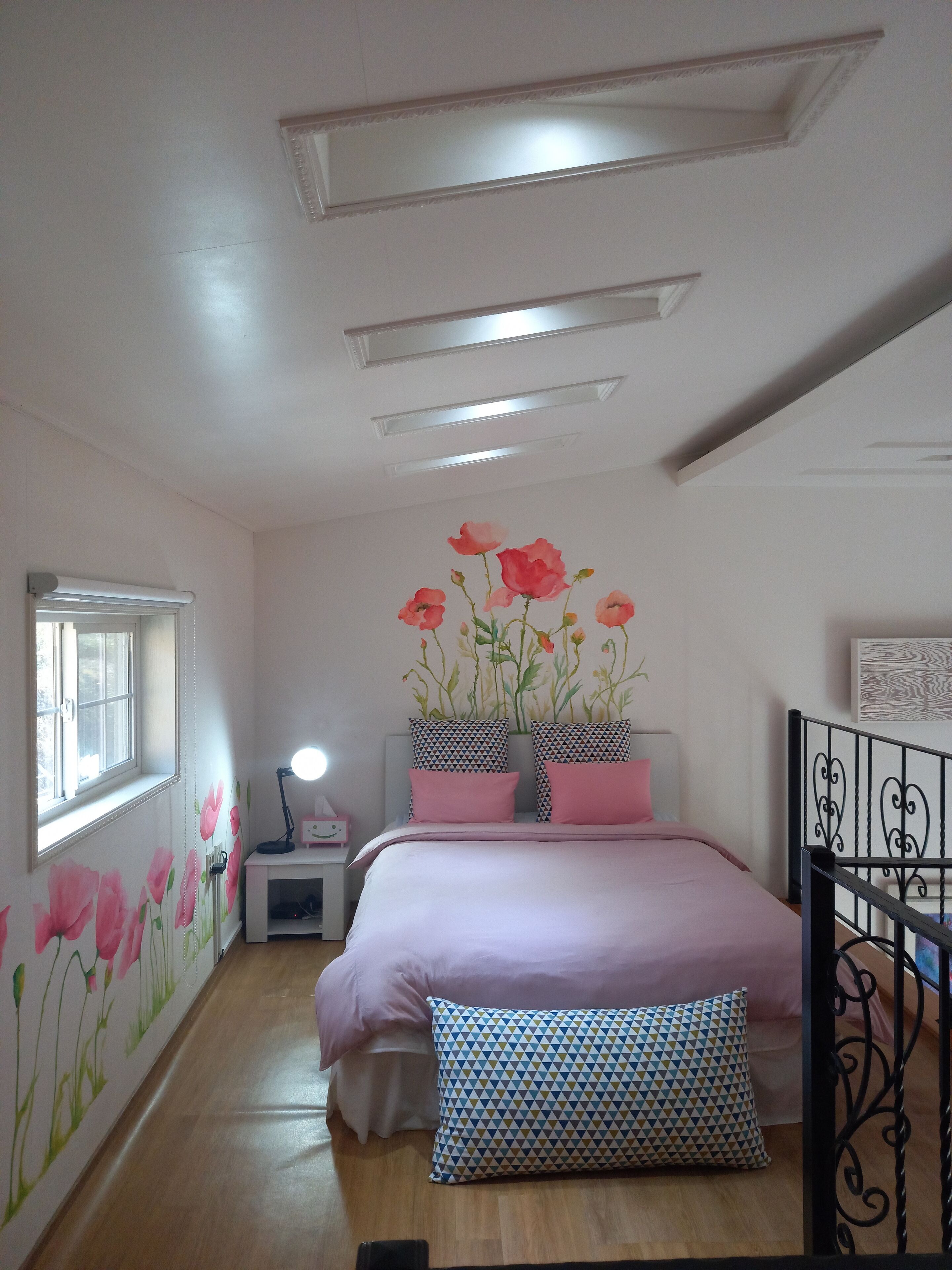 A bedroom with a bed, a nightstand, a lamp, a window, and a wall with floral wallpaper.