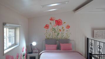 A bedroom with a bed, a nightstand, a lamp, a window, and a wall with floral wallpaper.