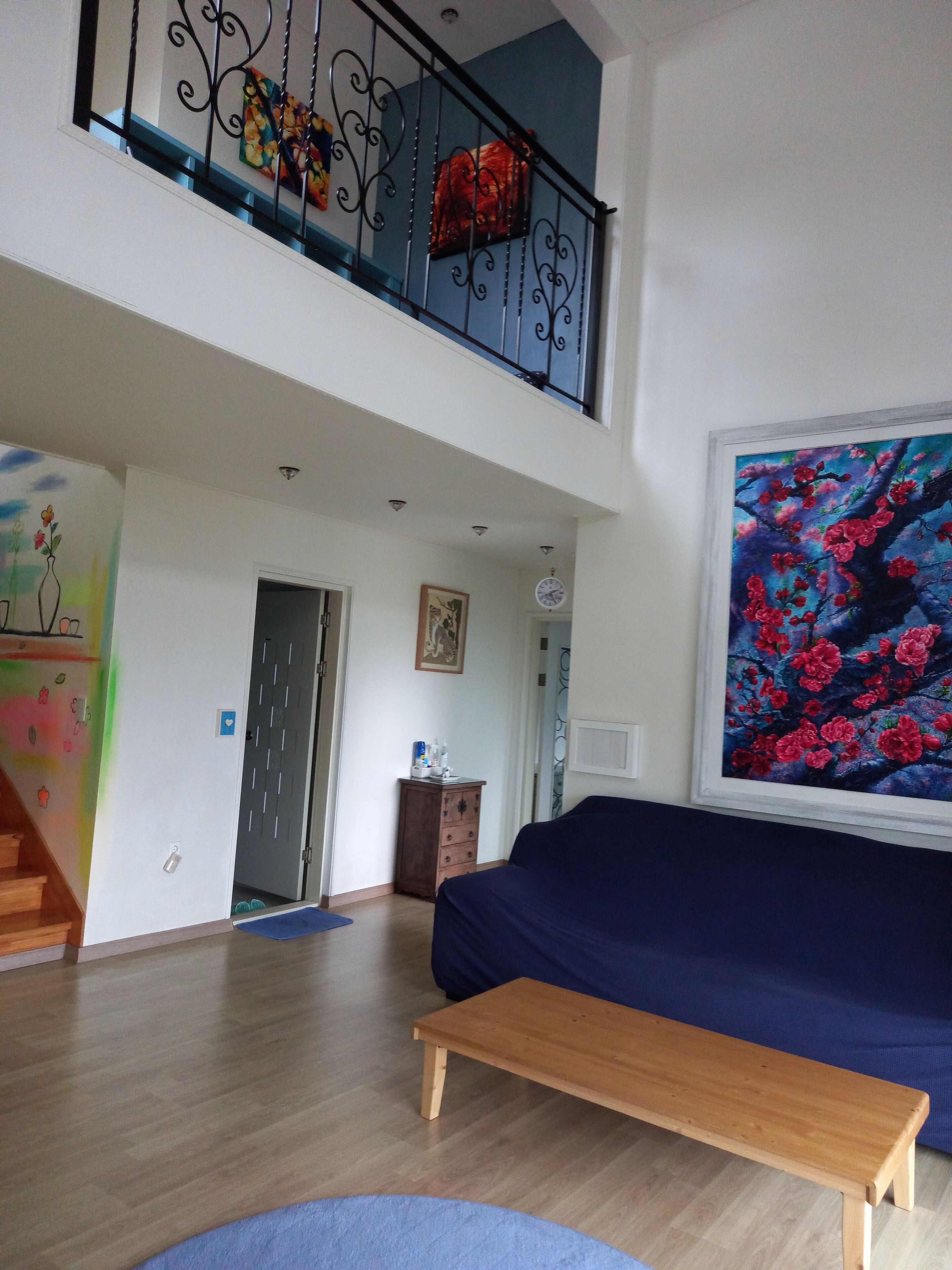 Ein geräumiges Wohnzimmer mit hoher Decke, einer hölzernen Bank, einem blauen Sofa und einem Gemälde mit roten Blumen.