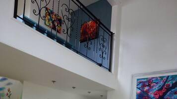 Ein geräumiges Wohnzimmer mit hoher Decke, einer hölzernen Bank, einem blauen Sofa und einem Gemälde mit roten Blumen.