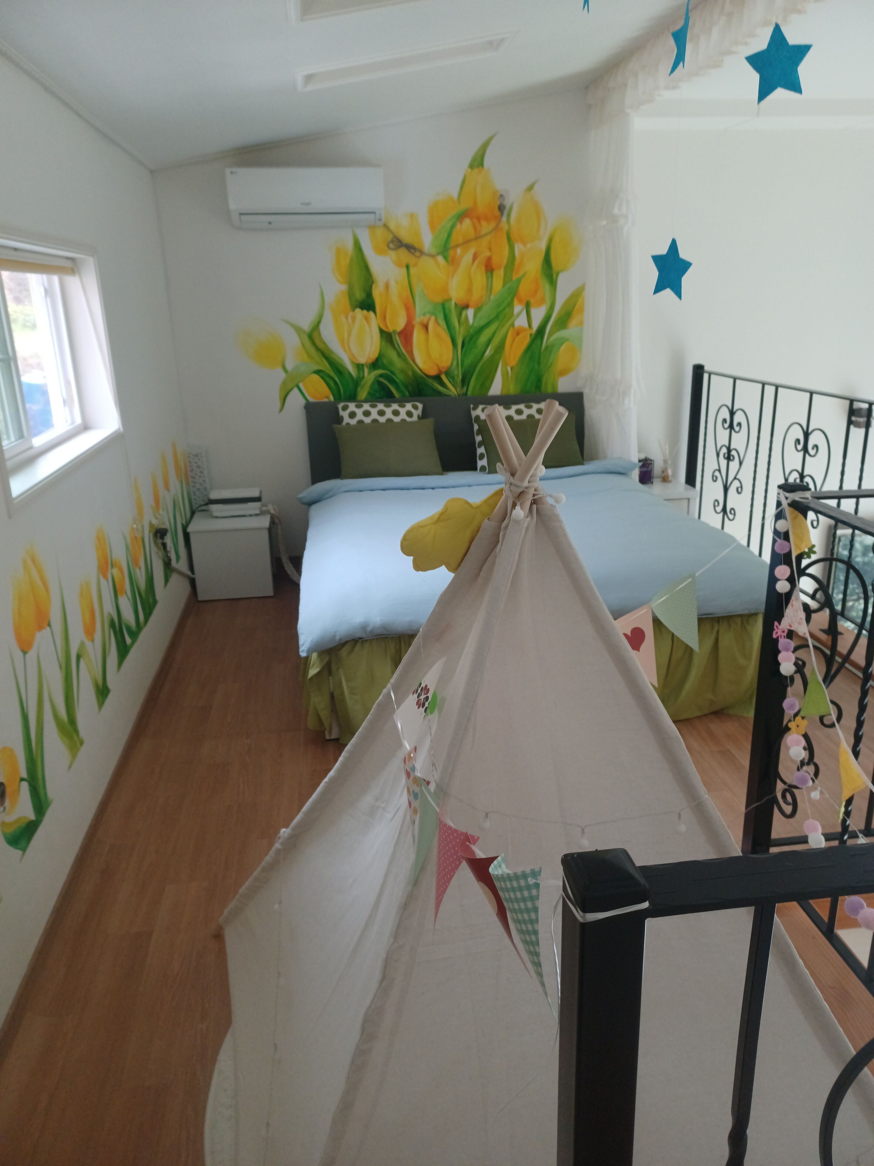 Un dormitorio con cama, ventana, un mural en la pared y una estructura similar a una tienda de campaña.