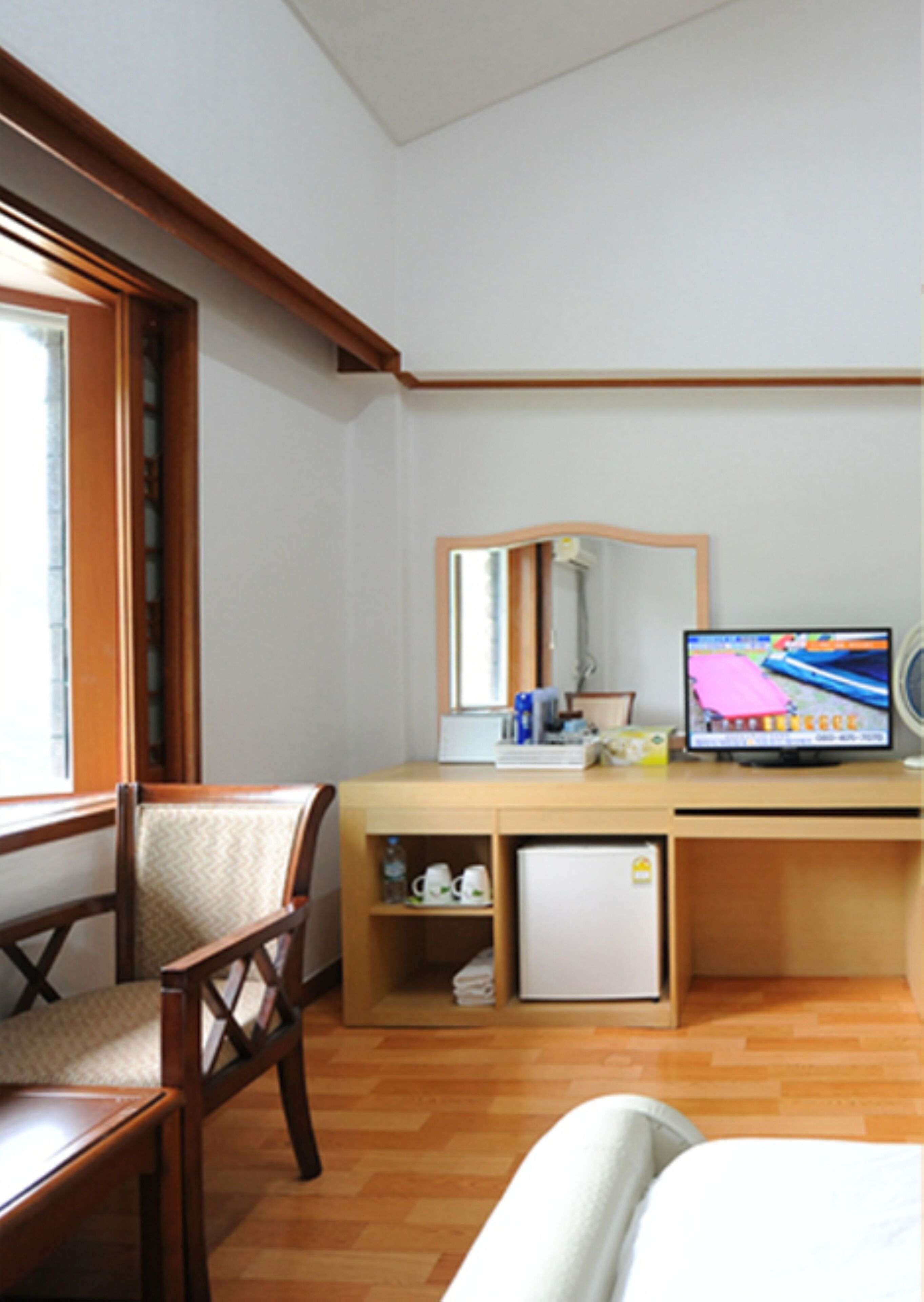Ein kleines Hotelzimmer mit einem Holztisch, einem kleinen Kühlschrank, einem Stuhl, einem Bett und einem Fernseher.