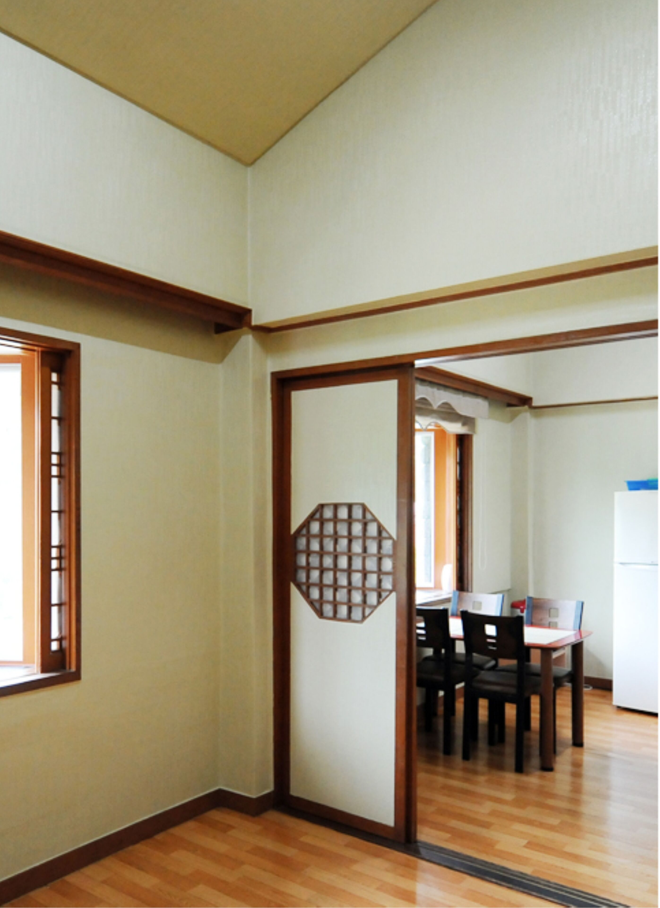Una habitación con suelo de madera, una mesa de comedor con sillas y un refrigerador blanco.