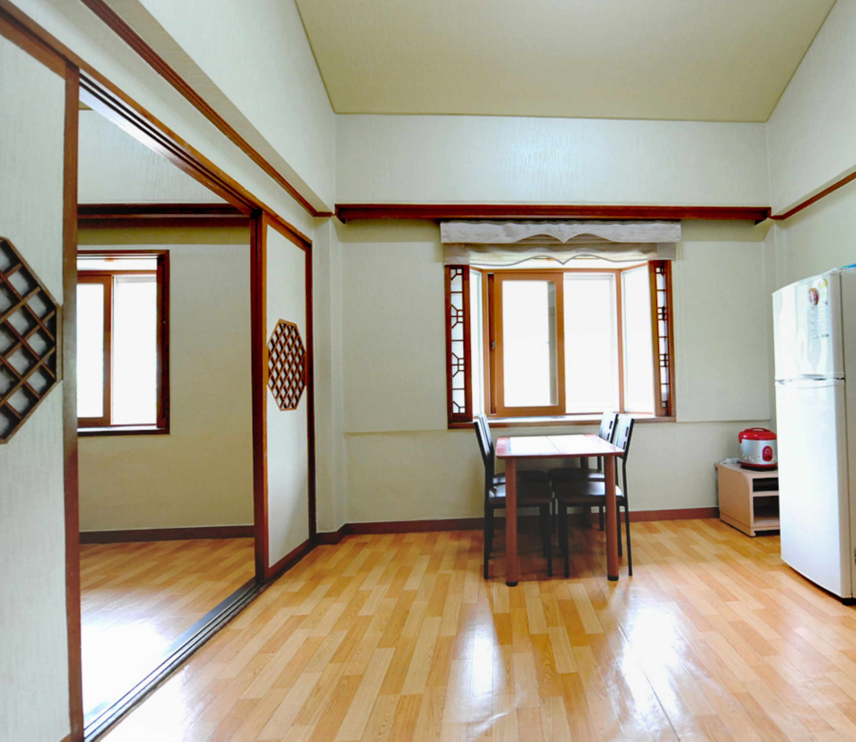 A spacious kitchen with wooden flooring, a dining table with chairs, a refrigerator, and a window with wooden shutters.