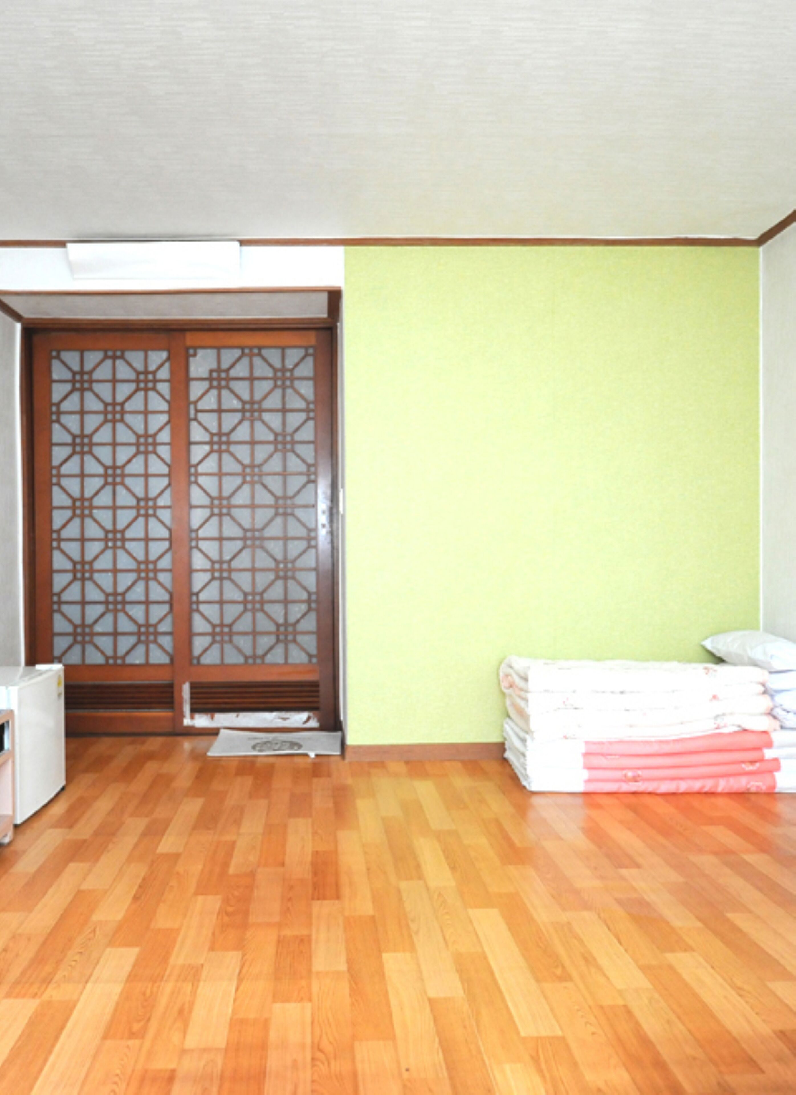 Quarto com piso de madeira, parede verde e porta deslizante tradicional com padrão geométrico.