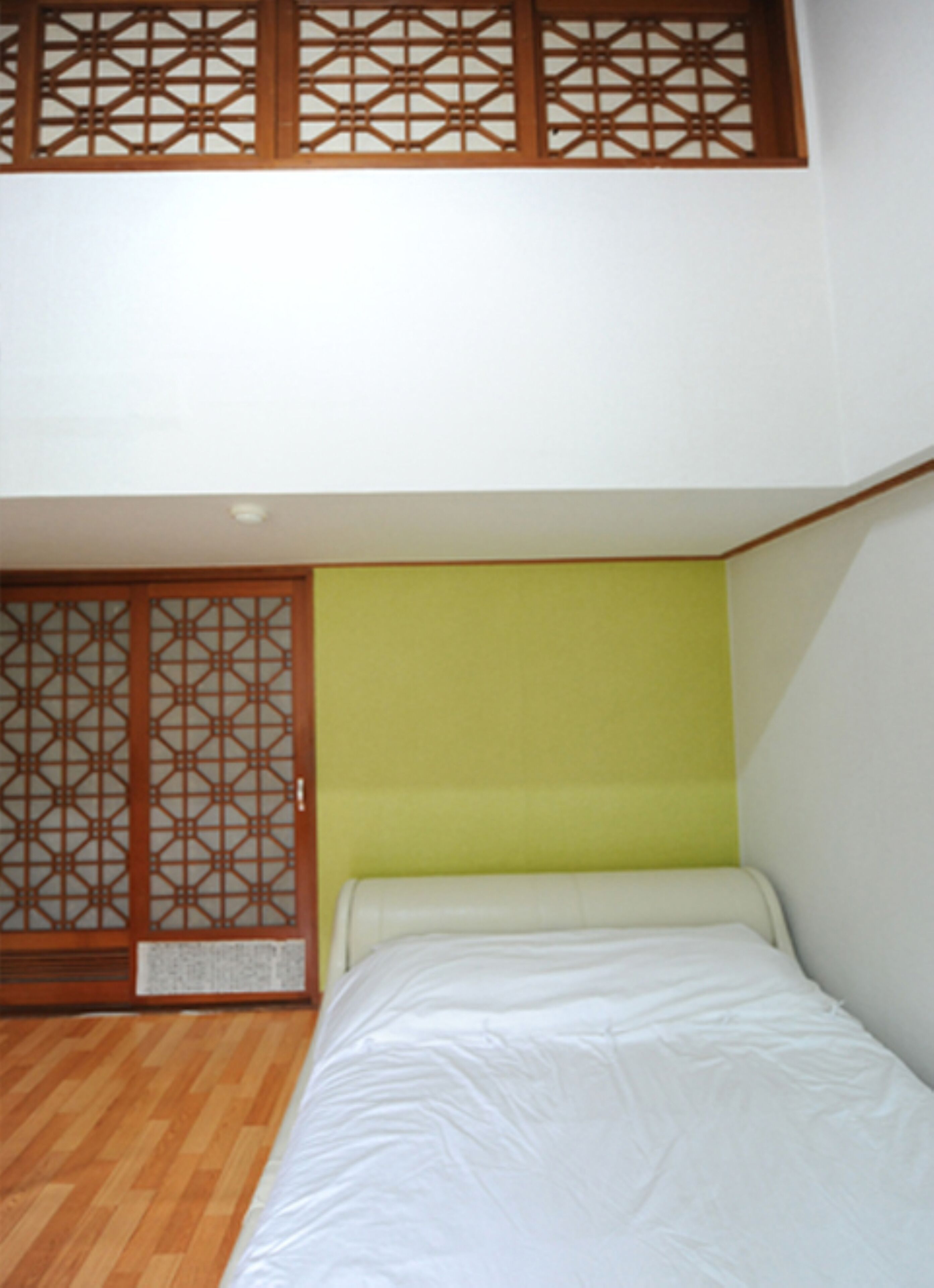 A room with a bed, a wooden sliding door, and a yellow wall.