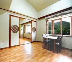 Una habitación con piso de madera, una mesa de comedor con sillas, vista a un bosque por una ventana y puertas correderas con diseños de celosía.
