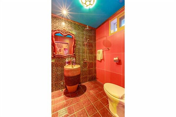 Un baño con piso de baldosas rojas, inodoro, lavamanos con espejo y ducha.