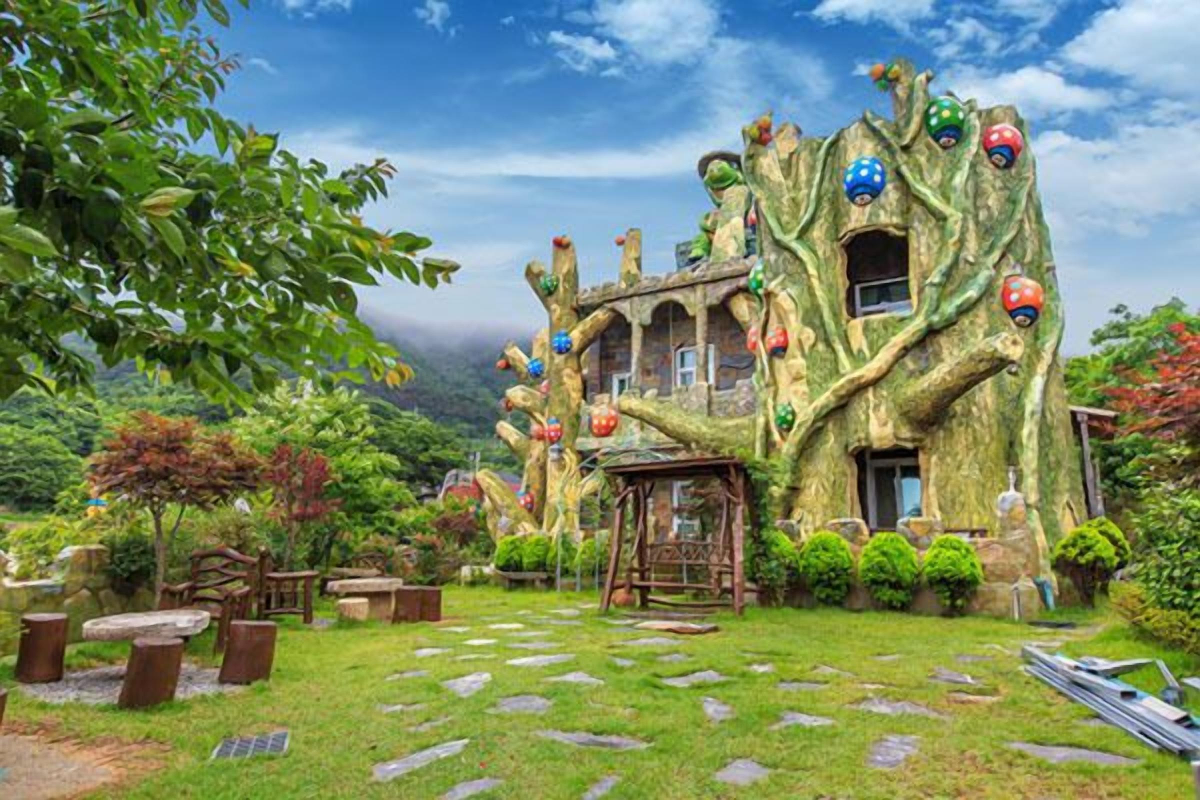 A treehouse with a rustic design, surrounded by lush greenery and a stone pathway.