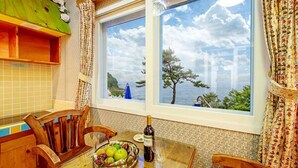 Un coin repas avec une table, des chaises, une bouteille de vin et un panier de fruits.
