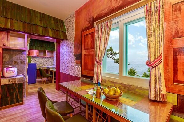 A cozy dining area with a glass table, chairs, and a view of the sea. - Yeonggwang Chezlee Pension (Yeonggwang)