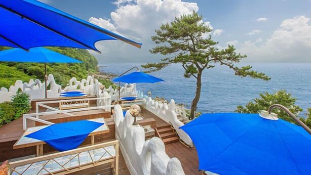 Une terrasse en bord de mer, agrémentée de parasols bleus, de rampes blanches et de tables en bois.