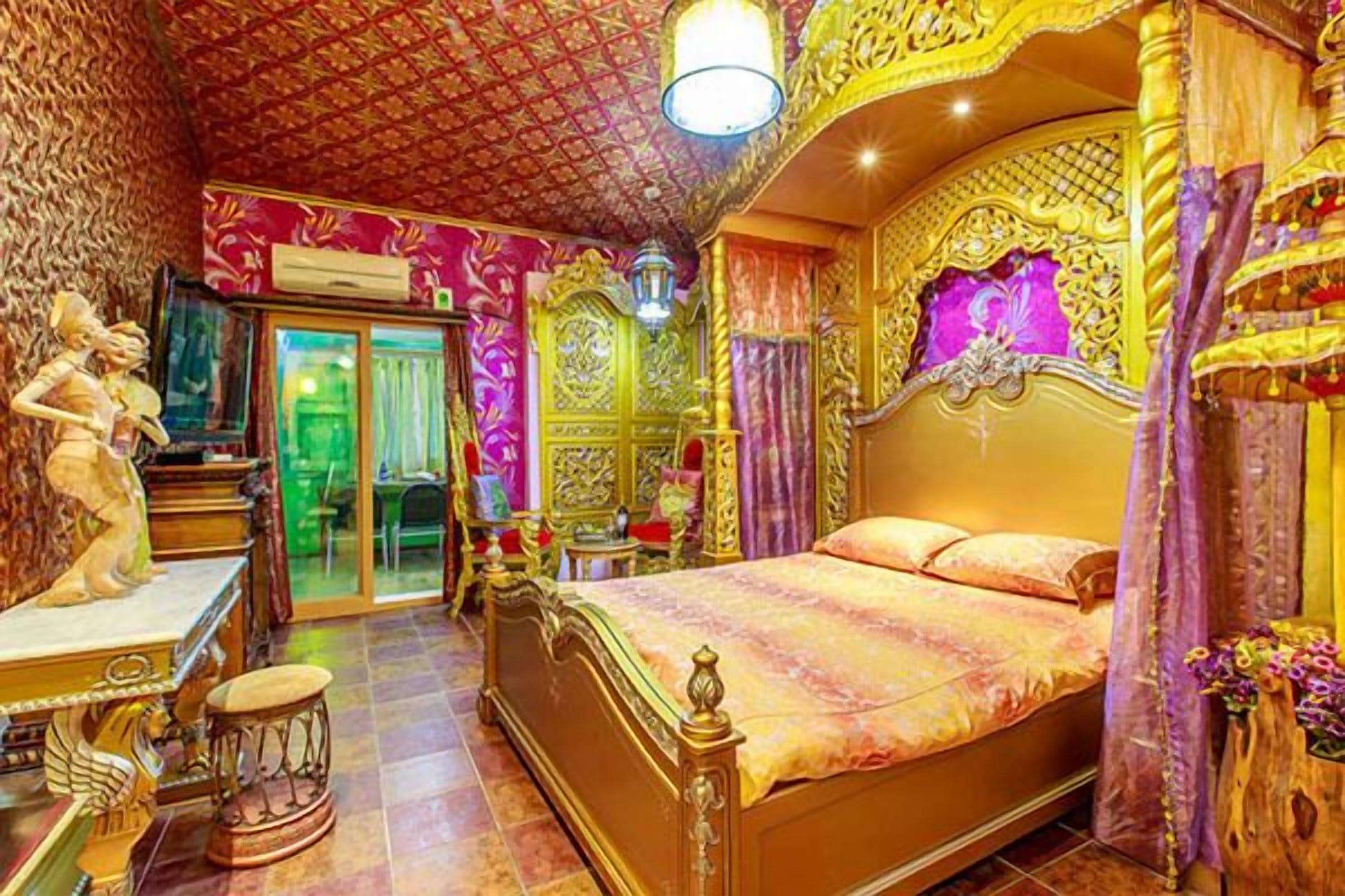 A luxurious bedroom with ornate golden decor, a large bed, and a statue on the left.