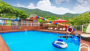 Une piscine avec un toboggan, des chaises longues et une vue sur des collines verdoyantes.