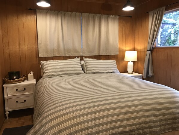A neatly made bed with striped bedding, a bedside lamp, and a nightstand with drawers. - Vintage Adelaida Home on 16 acres (Paso Robles)
