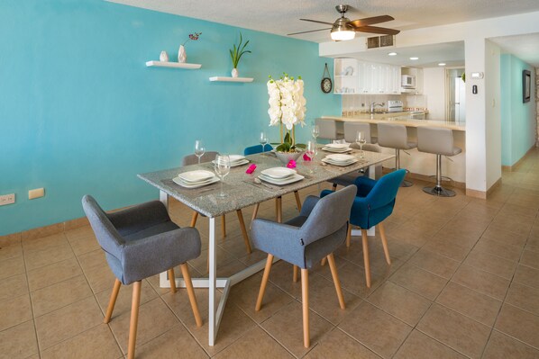 A dining area with a table set for four, surrounded by chairs, in a modern kitchen with white cabinets and a teal accent wall.