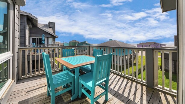 Eine Holzterrasse mit Tisch und Stühlen mit Blick auf eine Wohngegend, Häuser und einen klaren Himmel.