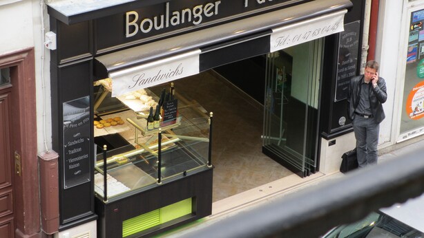 En butik med ett skyltfönster där det står ”Boulanger Pâtissier” och ett vitrinskåp med bröd.