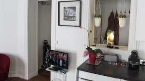 Ett vardagsrum med en tv, en röd fåtölj, en krukväxt och en inramad tavla på väggen.