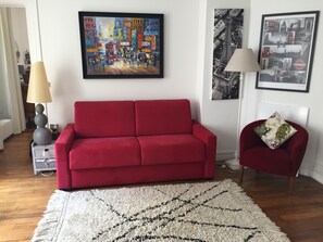 Un salon avec un canapé rouge, un tapis à poils longs blanc et deux tableaux encadrés accrochés au mur.