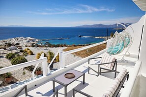 Una terraza con vista al mar, mobiliario blanco y plantas en macetas.