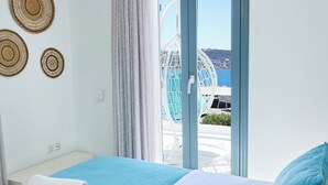 Habitación de hotel con cama, una cesta de toallas y vista al mar a través de un ventanal.
