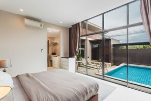 Et moderne hotelværelse med en stor seng, badeværelse med bruser, og udsigt til et udendørs poolområde.