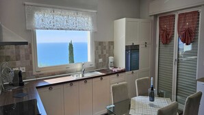 A modern kitchen with a view of the sea, a dining area with a table and chairs, and a refrigerator. - Beautiful apartment in Imperia Porto Maurizio, best panoramic area of the city (Imperia)