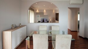 A modern dining area with a glass table, four upholstered chairs, a wooden sideboard, and a large mirror above the table. - Beautiful apartment in Imperia Porto Maurizio, best panoramic area of the city (Imperia)