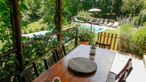 A wooden table with chairs, a lantern, and a potted plant in a garden setting with a pool and lounge chairs in the background. - Beautiful villa, private pool WIFI gorgeous gardens & mountain views- peaceful! (Poggio)