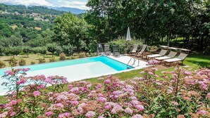 A swimming pool with a deck area, surrounded by lush greenery and flowering plants. - Beautiful villa, private pool WIFI gorgeous gardens & mountain views- peaceful! (Poggio)