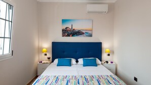 Hotellihuone, jossa on suuri sänky, kaksi yöpöytävalaisinta, majakan kuva seinällä ja ilmastointilaite seinässä.