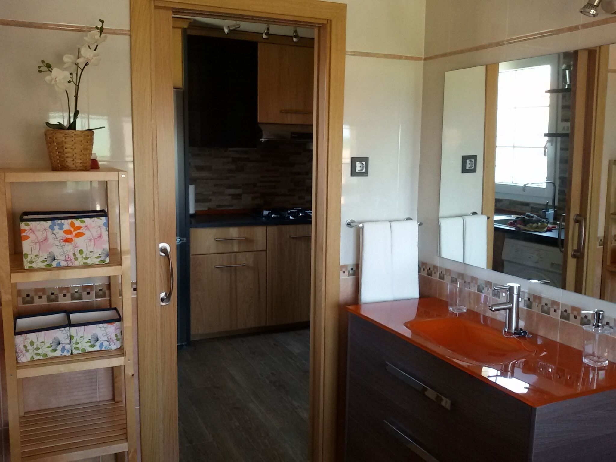 Ein modernes Badezimmer mit einem Holzkosmetikschrank, einem großen Spiegel und einem Waschbecken. Es gibt eine kleine Ablage mit einer dekorativen Schachtel und einer Topforchidee.